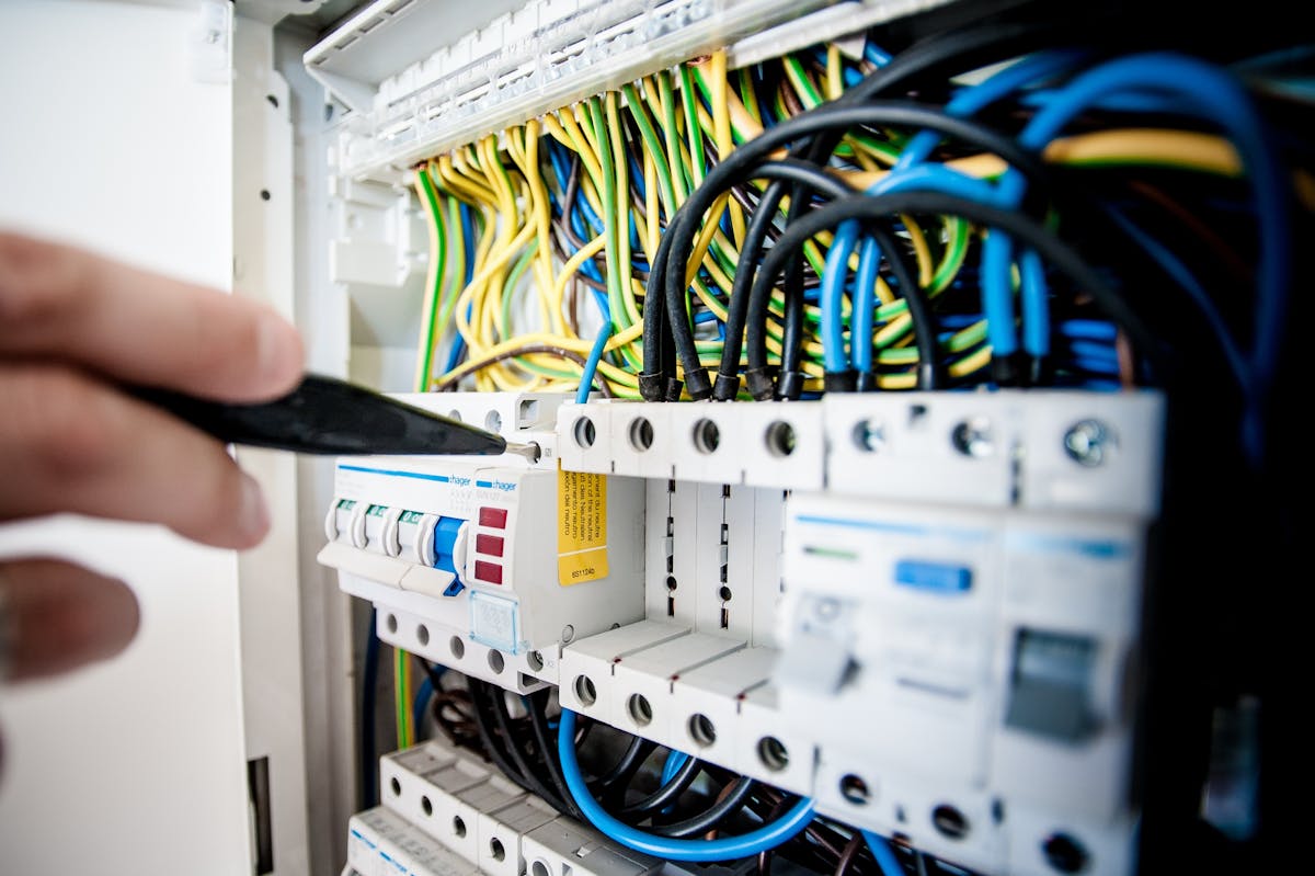 Elektriker arbetar koncentrerat vid en elcentral med professionella verktyg, kablar i prydliga rader